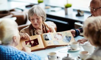 an elderly woman shows photos from a album to her friends