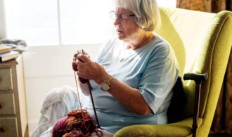 an elderly woman sits in a chair and knits