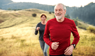 A senior living couple jog in front of a scenic hillscape